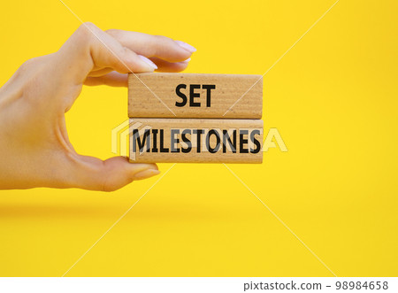 Set milestones symbol. Concept word Set milestones on wooden blocks. Beautiful yellow background. Businessman hand. Business and Set milestones concept. Copy space Set milestones symbol. Concept word Set milestones on wooden blocks. Beautiful yellow background. Businessman hand. Business and Set milestones concept. Copy space 98984658