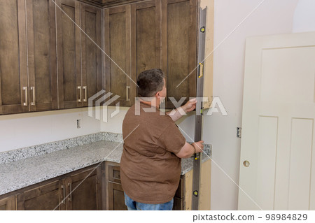 Worker holding level for leveling of new kitchen cabinets before it was installed with its furniture set Worker holding level for leveling of new kitchen cabinets before it was installed with its furniture set 98984829