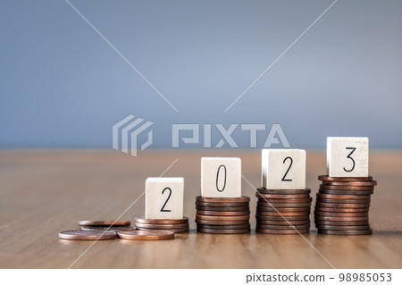 wooden cube year 2023 on top stack of coins with sky blue background and copy space. saving money and financial plan concept for investment in new year 2023. 98985053