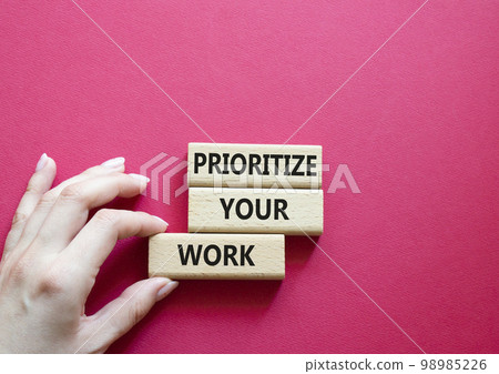 Priority symbol. Wooden blocks with words 'Prioritize your work'. Beautiful red background. Businessman hand. Business and 'Prioritize your work' concept. Copy space. 98985226