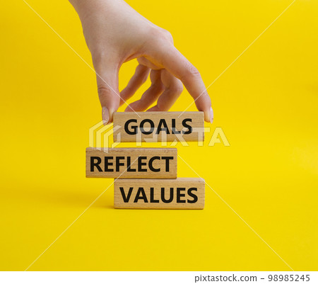 Goals reflect values symbol. Concept words Goals reflect values on wooden blocks. Beautiful yellow background. Businessman hand. Business and Goals reflect values concept. Copy space Goals reflect values symbol. Concept words Goals reflect values on wooden blocks. Beautiful yellow background. Businessman hand. Business and Goals reflect values concept. Copy space 98985245