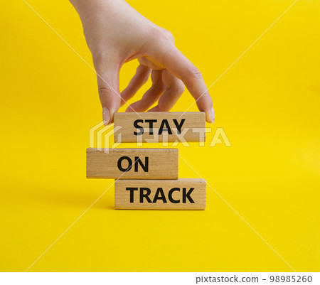 Stay on track symbol. Wooden blocks with words 'Stay on track'. Beautiful yellow background. Businessman hand. Business and 'Stay on track' concept. Copy space. 98985260