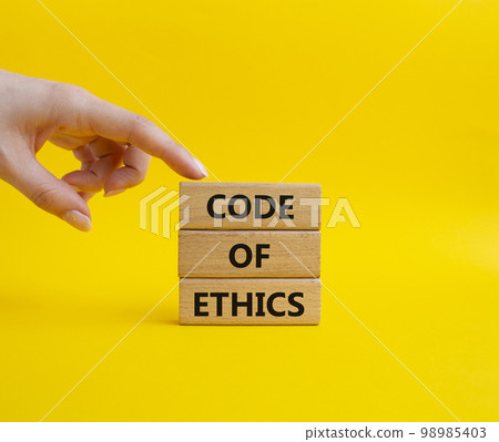 Code of ethics symbol. Concept words Code of ethics on wooden blocks. Beautiful yellow background. Businessman hand. Business and Code of ethics concept. Copy space. Code of ethics symbol. Concept words Code of ethics on wooden blocks. Beautiful yellow background. Businessman hand. Business and Code of ethics concept. Copy space. 98985403