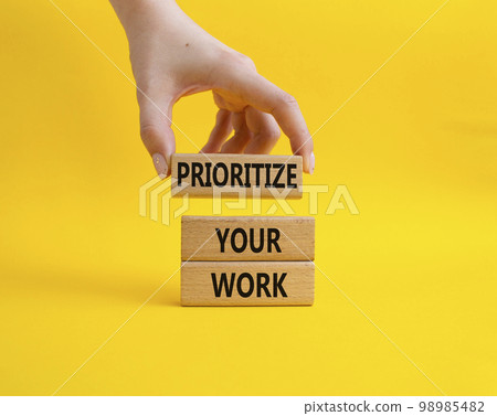Priority symbol. Wooden blocks with words 'Prioritize your work'. Beautiful yellow background. Businessman hand. Business and 'Prioritize your work' concept. Copy space. 98985482