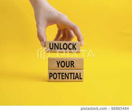 Unlock your Potential symbol. Wooden blocks with words Unlock your Potential. Beautiful yellow background. Businessman hand. Business and Unlock your Potential concept. Copy space. 98985484