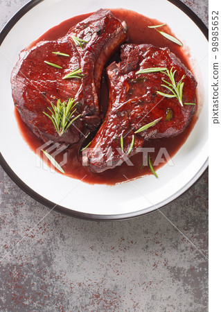 Pork chops on the bone fried and then cooked with red wine, herbs and spices close-up on a plate. Vertical top view 98985652