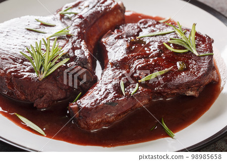 Pork chops on the bone fried and then cooked with red wine, herbs and spices close-up on a plate. Horizontal 98985658