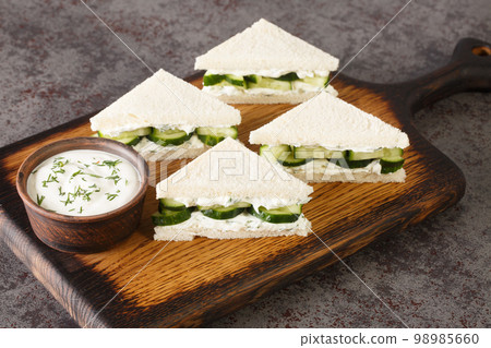 Cucumber Sandwiches are a made with layers of thin cucumbers and fresh herbed cream cheese closeup on the wooden board. Horizontal 98985660