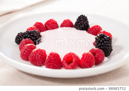 fresh raspberries and blackberries laid out on a white plate in circle with yogurt fresh raspberries and blackberries laid out on a white plate in circle with yogurt 98985752