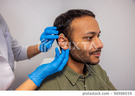 ENT doctor implementing hearing aid to the patients ear 98986039