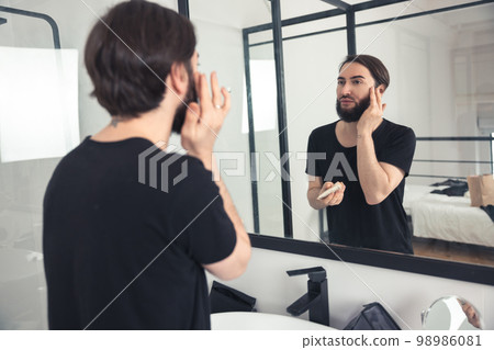 Bearded guy applying cosmetics to his face 98986081