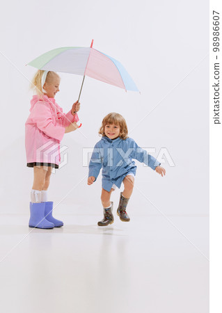 Cute children, happy kids in raincoats playing, having fun together isolated over white background. Concept of childhood, friendship, family, fun, active lifestyle, fashion Cute children, happy kids in raincoats playing, having fun together isolated over white background. Concept of childhood, friendship, family, fun, active lifestyle, fashion 98986607