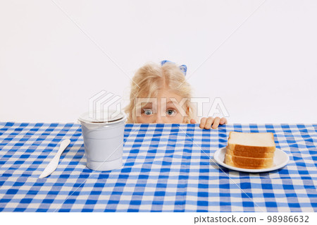Little cute girl looks out from behind table with fear in her eyes isolated over white studio background. Concept of childhood, emotions, lifestyle, surprise, facial expression 98986632