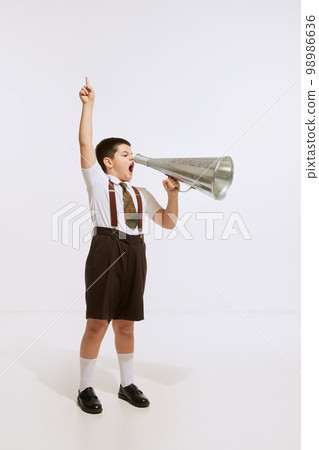 One preschool age kid wearing retro style shorts with suspenders shouting at megaphone isolated over white background. Concept of emotions, childhood, news 98986636