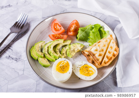 Avocado, soft boiled egg, tomatoes, lettuce and toast on a plate. Healthy food. Avocado, soft boiled egg, tomatoes, lettuce and toast on a plate. Healthy food. 98986957
