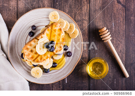 Banana, blueberry and honey toasts on a plate. Homemade dessert. Top view 98986968