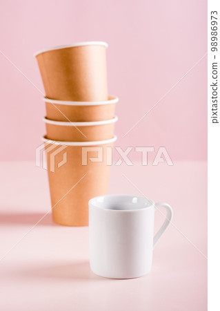 The concept of choosing between a ceramic and paper coffee cup. Reusable tableware. Vertical view The concept of choosing between a ceramic and paper coffee cup. Reusable tableware. Vertical view 98986973