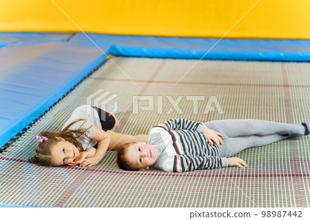 Happy smiling small kids laying on indoor trampoline in entertainment center Happy smiling small kids laying on indoor trampoline in entertainment center 98987442