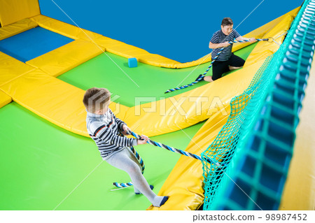 Kids playing in trampoline center jumping and climbing with rope Kids playing in trampoline center jumping and climbing with rope 98987452