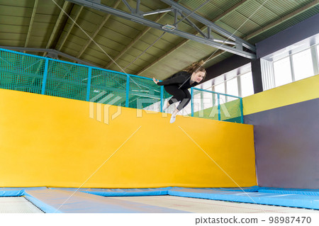 Young woman amateur acrobatic athlete jumping and exercising on a trampoline indoors, modern hobby and fitness concept 98987470