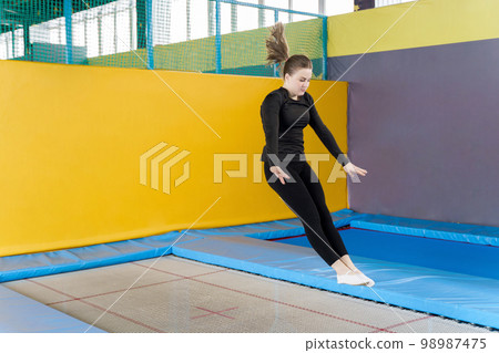 Teenage girl jumping on trampoline in fitness center Teenage girl jumping on trampoline in fitness center 98987475