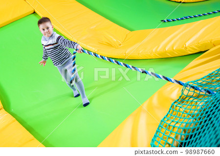 Little boy playing in trampoline center jumping and climbing with rope Little boy playing in trampoline center jumping and climbing with rope 98987660