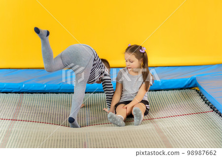 Happy smiling small kids sitting on indoor trampoline and playing in entertainment center Happy smiling small kids sitting on indoor trampoline and playing in entertainment center 98987662