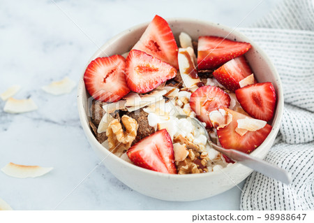 Cottage cheese bowl with strawberries, cereal flakes, coconut, nuts and syrup, marble background. Cottage cheese bowl with strawberries, cereal flakes, coconut, nuts and syrup, marble background. 98988647