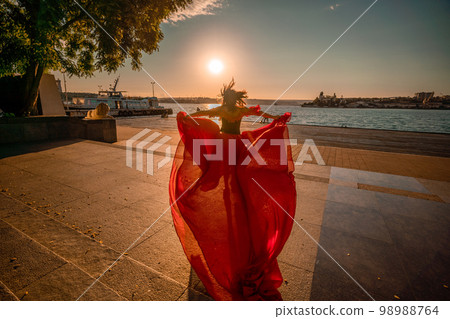 Sunrise red dress. A woman in a long red dress against the backdrop of sunrise, bright golden light of the sun's rays. The concept of femininity, harmony. 98988764