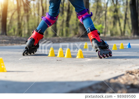 Group of little children enjoy having fun learning inline roller skate slalom with plastic cones on road in city park outdoors on sunny spring day. Healthy kid outside sport exercise activities 98989500