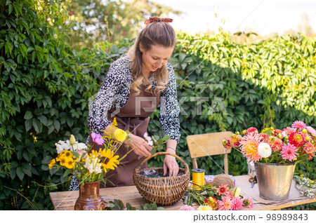 A florist girl collects a bouquet of autumn flowers in a basket 98989843