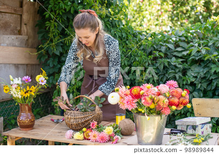 A florist girl collects a bouquet of autumn flowers in a basket 98989844