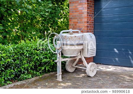 A white old concrete mixer near the garage entrance. A white old concrete mixer near the garage entrance. 98990618
