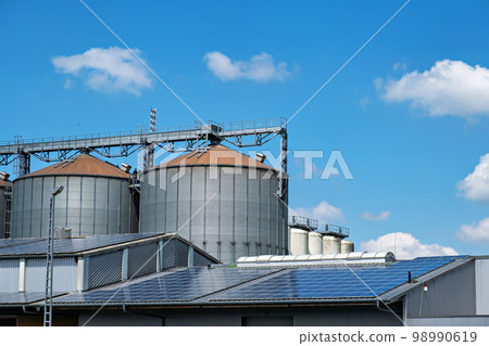 Close-up of silver silos at an agro-processing plant for processing, drying, cleaning and storing agricultural products and solar panels. Close-up of silver silos at an agro-processing plant for processing, drying, cleaning and storing agricultural products and solar panels. 98990619