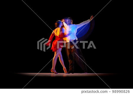 Expressive artistic young man and woman dancing tango, ballroom over black background with mixed neon lights. Concept of art, beauty, motion Expressive artistic young man and woman dancing tango, ballroom over black background with mixed neon lights. Concept of art, beauty, motion 98990826