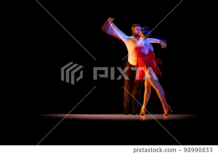 Expressive artistic young man and woman dancing tango, ballroom over black background with mixed neon lights. Concept of art, beauty, motion Expressive artistic young man and woman dancing tango, ballroom over black background with mixed neon lights. Concept of art, beauty, motion 98990833