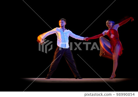 Man and woman, professional dancers in stylish stage costumes performing ballroom, tango over black background with mixed neon lights. Concept of art, beauty, motion Man and woman, professional dancers in stylish stage costumes performing ballroom, tango over black background with mixed neon lights. Concept of art, beauty, motion 98990854