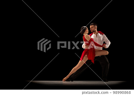 Talented performers. Beautiful young people, man and woman in classical ballroom stage costumes dancing tango over black studio background. Concept of art, beauty, motion Talented performers. Beautiful young people, man and woman in classical ballroom stage costumes dancing tango over black studio background. Concept of art, beauty, motion 98990868