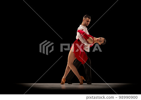 Attraction. Young man and woman, professional ballroom dancers, dancing tango over black background. Concept of art, beauty, motion Attraction. Young man and woman, professional ballroom dancers, dancing tango over black background. Concept of art, beauty, motion 98990900