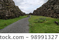 People walking down a path through the geological fault in Thingvellir National Park, Iceland 98991327