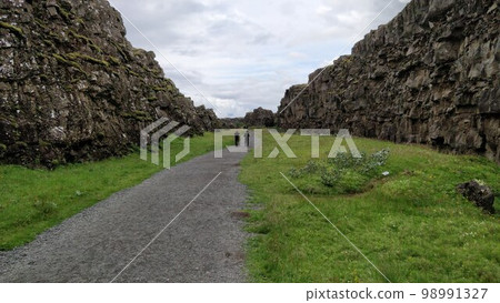 People walking down a path through the geological fault in Thingvellir National Park, Iceland 98991327