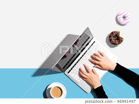 Person using a laptop computer with a donut and a cup of coffee Person using a laptop computer with a donut and a cup of coffee 98991497