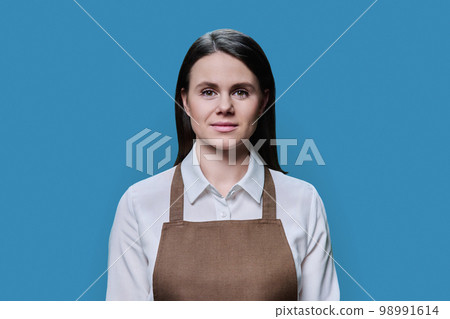 Portrait of young woman in an apron on blue background 98991614