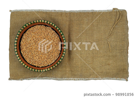 Wheat in a clay plate stands on a rural bag. Top view. Wheat in a clay plate stands on a rural bag. Top view. 98991856