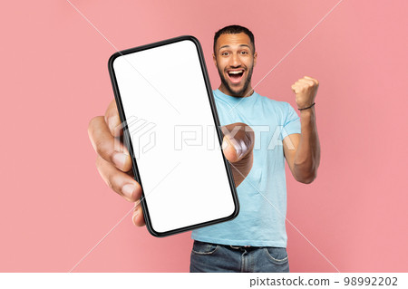 Big luck. Overjoyed black man holding big smartphone, showing empty screen and shaking clenched fist, mock up collage 98992202