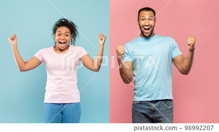 Euphoric black couple shaking clenched fists, exclaiming with excitement, standing over halved pink and blue background Euphoric black couple shaking clenched fists, exclaiming with excitement, standing over halved pink and blue background 98992207
