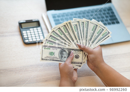 Woman hands holding dollar bills, working on laptop 98992260