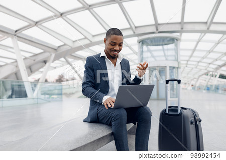 Remote Communication. Smiling Black Businessman At Airport Making Video Call On Laptop Remote Communication. Smiling Black Businessman At Airport Making Video Call On Laptop 98992454
