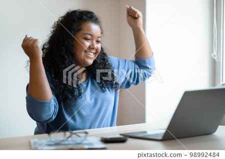 Emotional happy young chubby woman working from home, using laptop 98992484