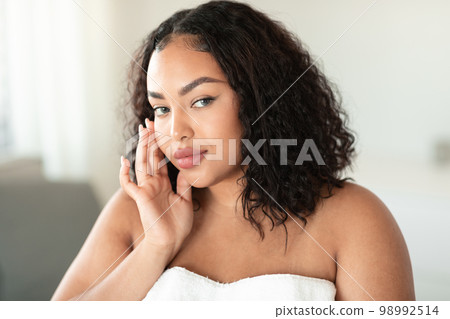 Beautiful black plus size woman touching face and looking at camera, body positive woman with flawless skin 98992514